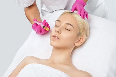 vampire facial® atlanta, image of a young blonde woman receiving an injection on the right side of her face.