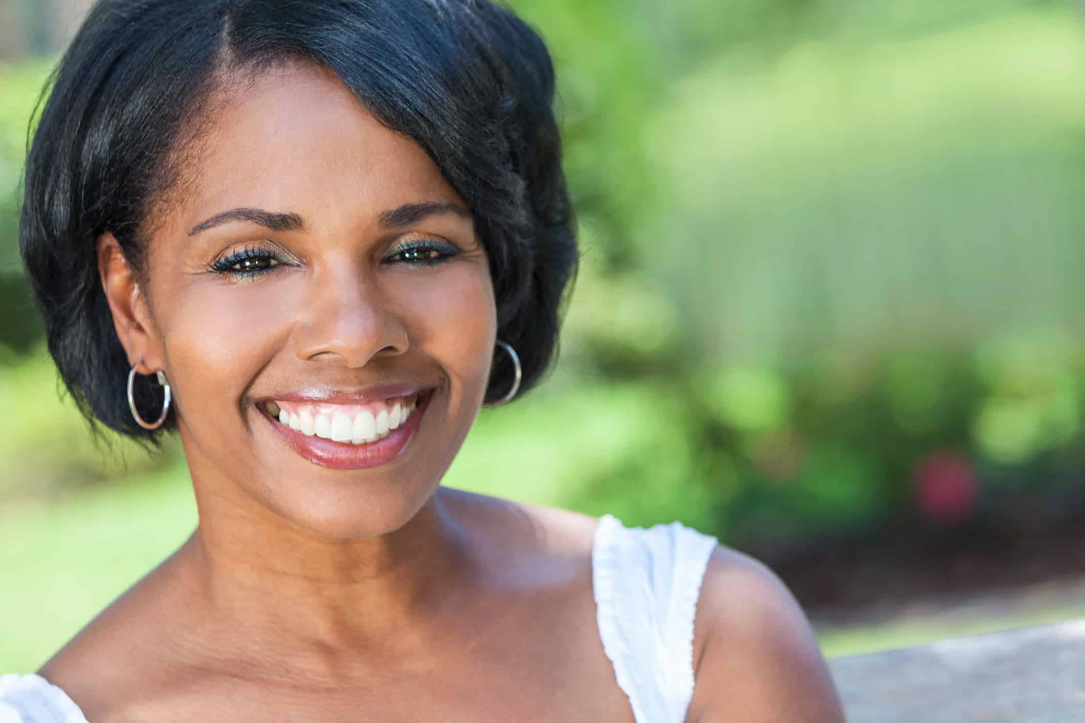 juvederm atlanta, image of a smiling middle aged woman with short black hair and wearing a white tank top with green landscape behind her.