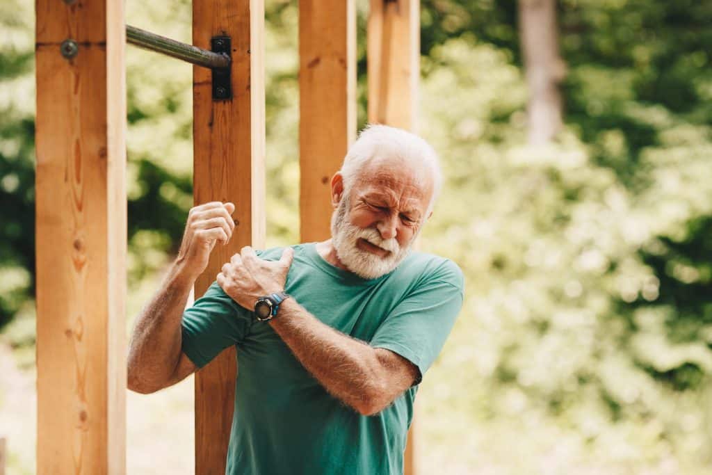 joint pain treatment Old man in green tshirt elevating his right arm and grasping his right shoulder with his left hand