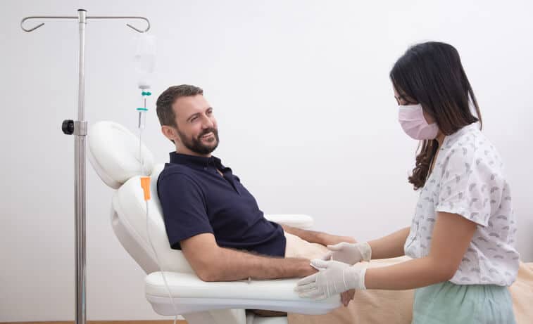 ozone therapy atlanta, image of a happy man sitting in a reclined doctor’s office chair about to receive IV treatment looks at the female nurse.