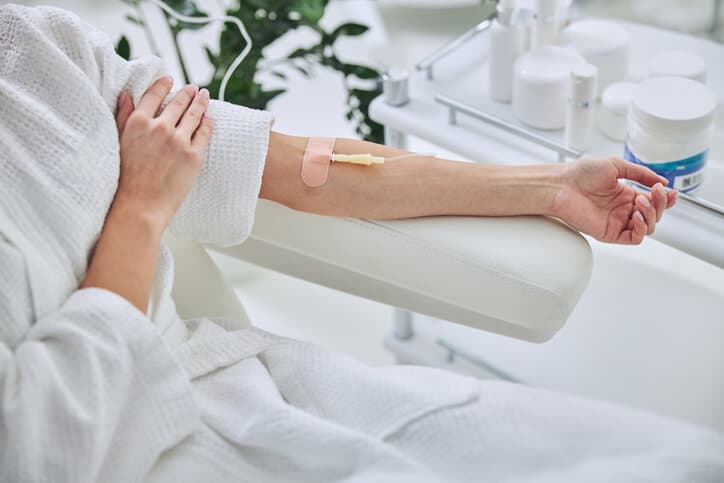 ozone therapy atlanta, image of a woman wearing a white robe, sitting in a reclining chair, extends her left arm out on the arm rest with an IV inserted in her arm.
