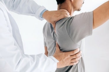 shoulder joint pain, image of a doctor grasping a male patient’s right shoulder with both of their hands.