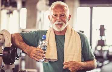 ozone therapy atlanta, image of an older man standing at the gym with a towel around his neck, holding a water bottle with right hand.