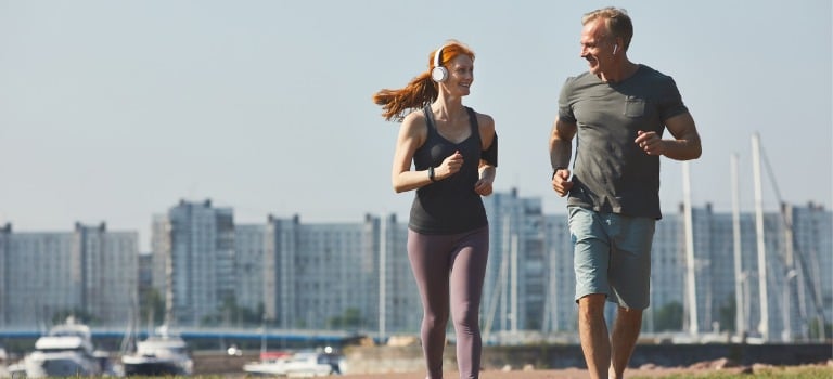 Knee Pain Specialists Woman and man couple jogging next to eachother and looking at eachother with high rise buildings behind them in the distance