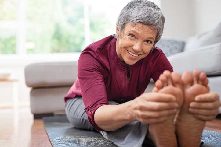 atlanta ankle and foot, woman with gray hair smiling while sitting down in a yoga outfit and stretching, grasping the balls of her feet