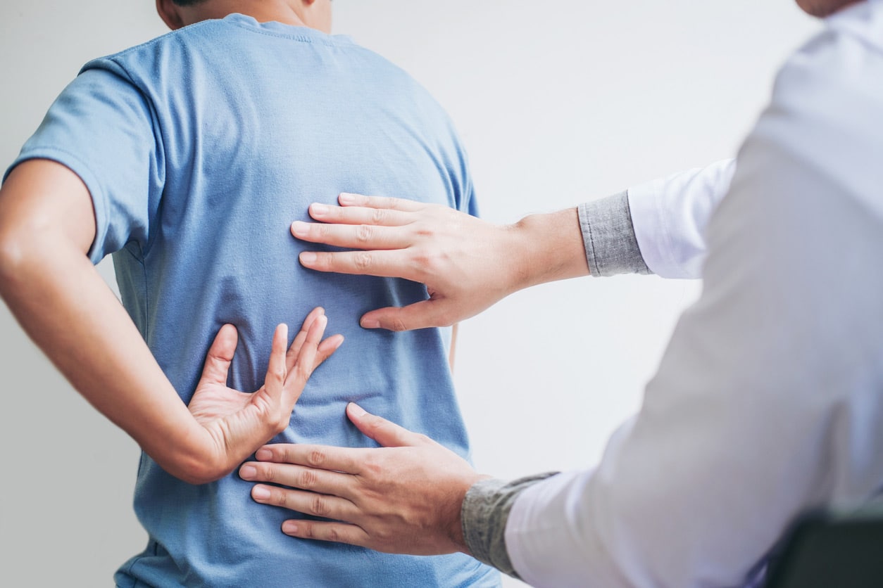 sciatica treatment specialist, image of a physician inspecting a male patient’s back with both hands.