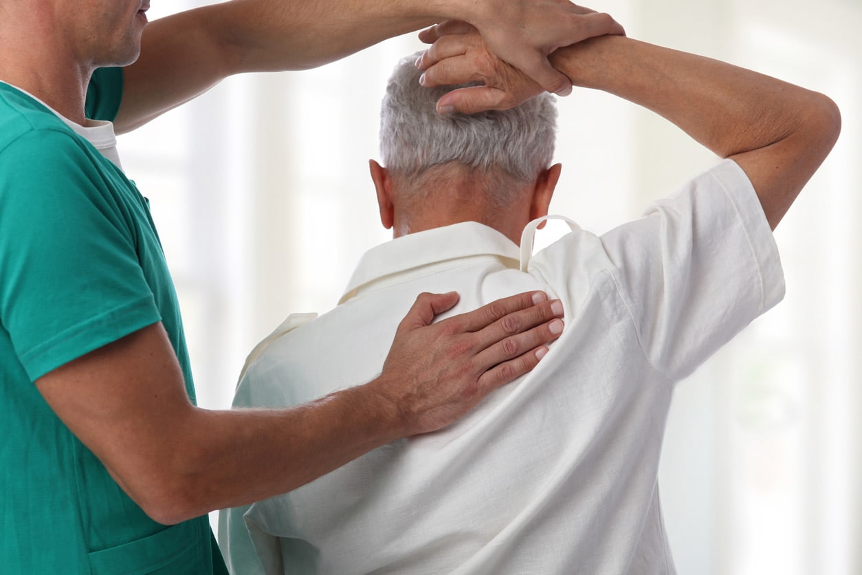 sciatica treatment specialist, image of a physician helping an older male patient lift his right arm above his head.