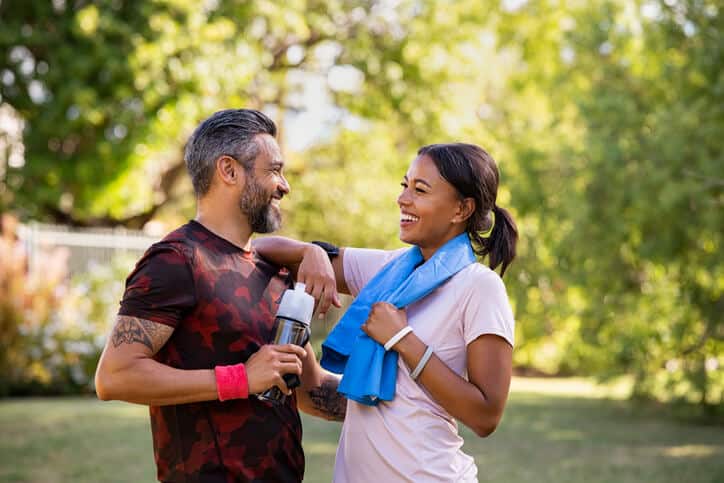 Trigger Point Injections, A smiling man wearing athletic clothing, holding a water bottle with his right hand faces a smiling woman wearing athletic clothing and a blue towel around her neck as she rests her right arm on the man's left shoulder
