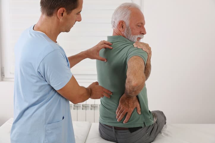 spinal stenosis treatment, image of a male physician using both hands to examine an elderly male patient’s back.