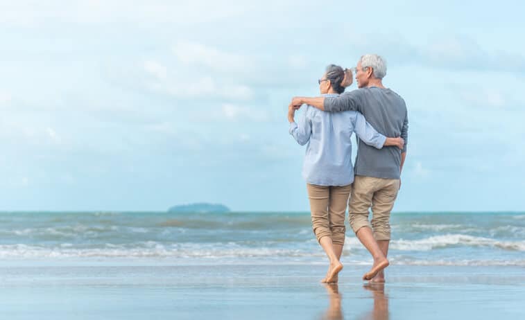 Prolotherapy, Older man and woman couple facing the ocean, walking on the beach and embracing eachother