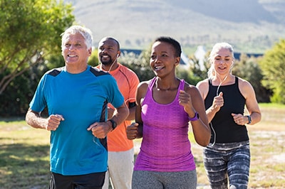 back pain specialists & doctors group of four middle aged people wearing workout gear running together in a field with mountains in the background