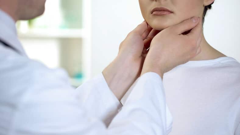 neck pain and headache relief Man medical practictioner wearing a white lab coat examines female patient's neck with both hands on her neck