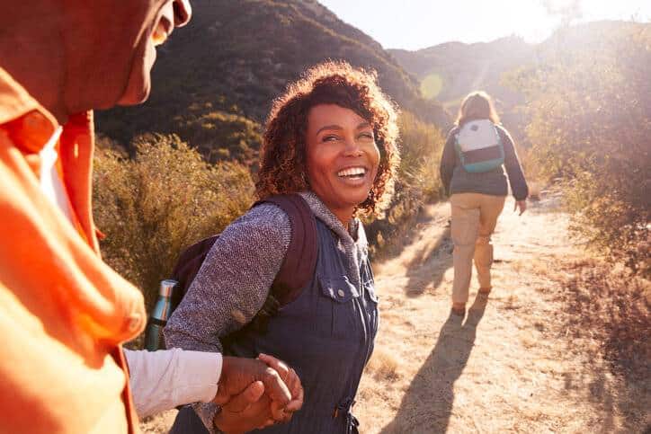 Prolozone Therapy, In the foreground a happy man and woman couple hold hands while walking together on a dirt path in the mountains. Ahead of them is another woman walking the dirt path