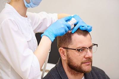 prp hair treatment atlanta, image of a man wearing glasses receiving PRP hair restoration treatment on the top right side of his head, administered by a female physician.