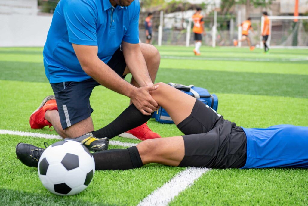 PRP Orthopedics, Male soccer couch bent down on one knee clutching the right knee of a fallen soccer player