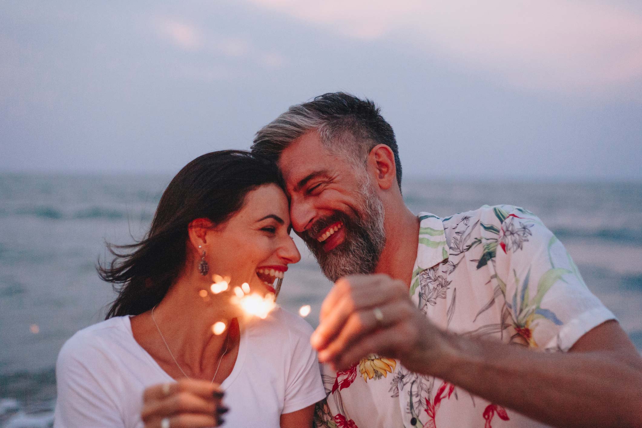 erectile dysfunction clinic, image of a happy couple touching foreheads and holding sparklers with the ocean behind them.