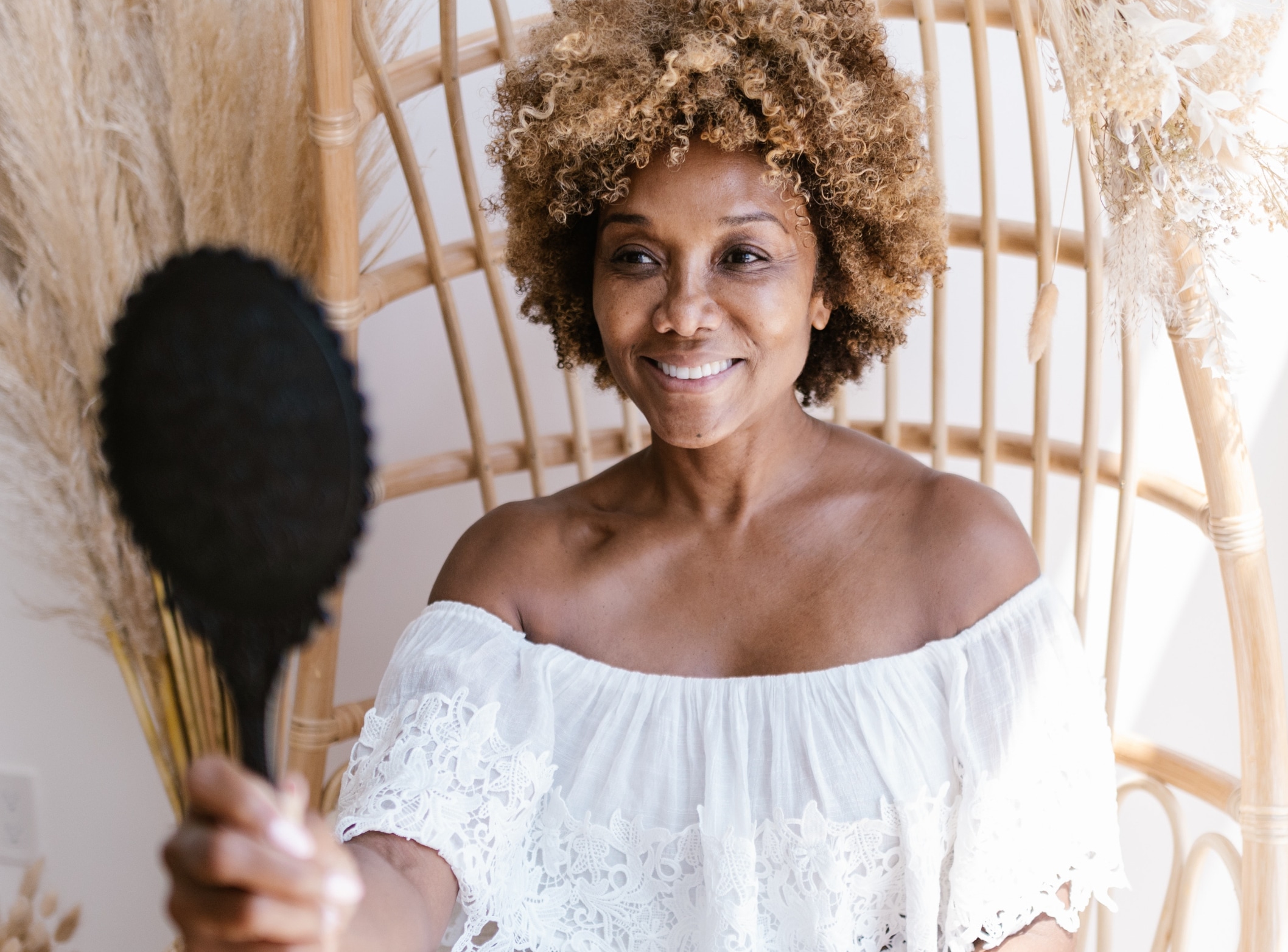 PRP For Facial Rejuvenation​, image of a middle aged woman sitting in a wicker chair and looking at herself in a hand-held mirror.