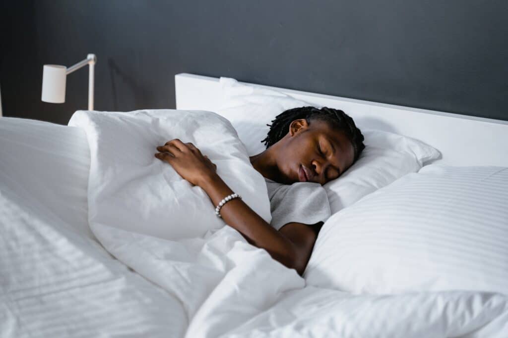 Lying in a bed with white bedding, a person is sleeping on their back, positioned to alleviate rotator cuff pain.