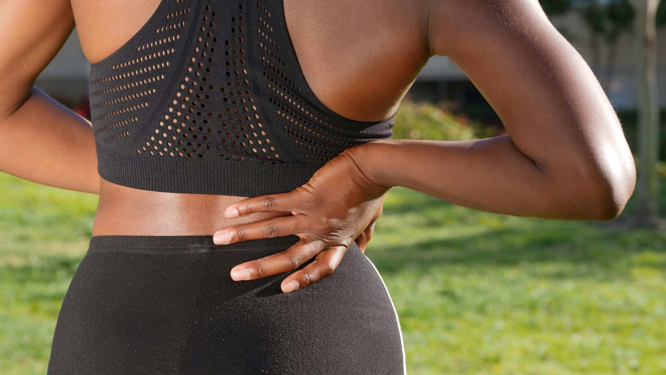 Up-close photo of a person wearing exercise clothes and holding their low back to suggest sciatica pain.