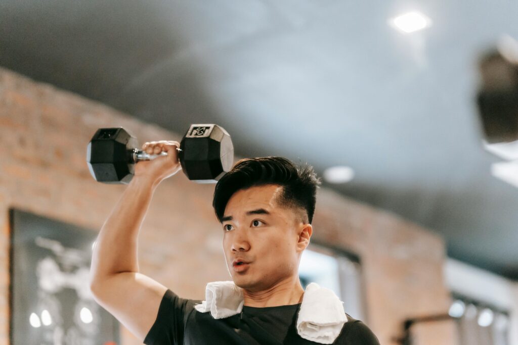Frozen shoulder; image of a man at the gym, lifting a large dumbbell in his right hand over his head.