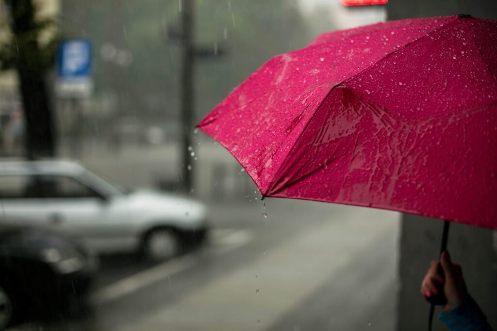 Arthritis Weather Index, image of a hand holding an open red umbrella on a city sidewalk.