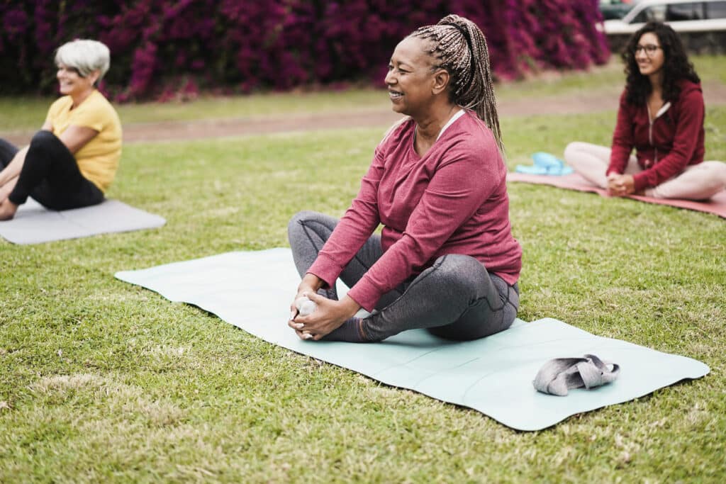 PRP injection for knee; image of three happy women doing a yoga pose in an outdoor yoga class.