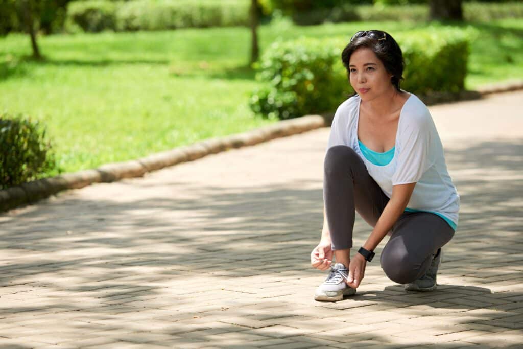 PRP injection for knee; image of a woman in the park kneeling down to tie her sneaker on her right foot.