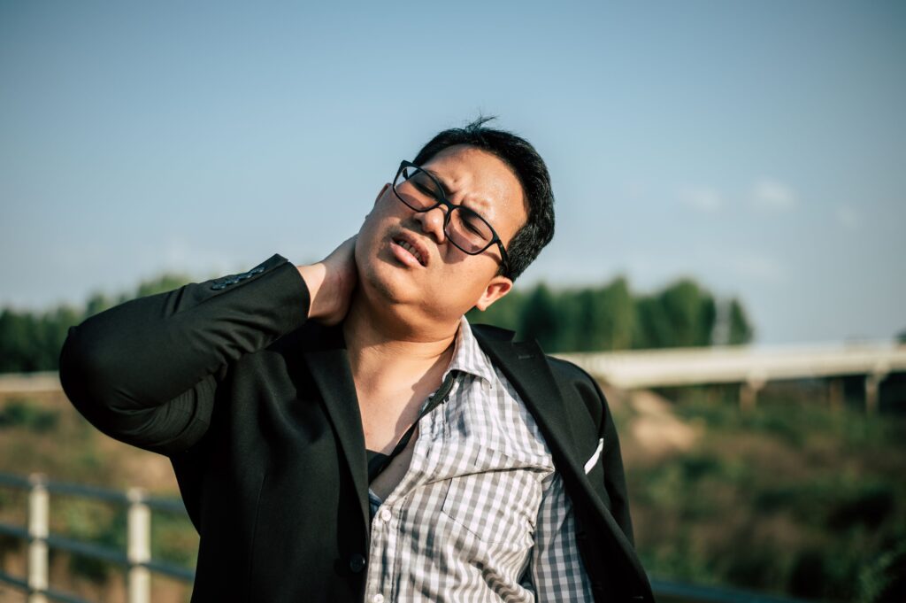 neck pain from sleeping, Image of a man in professional work clothes in pain, grasping his neck with his right hand.