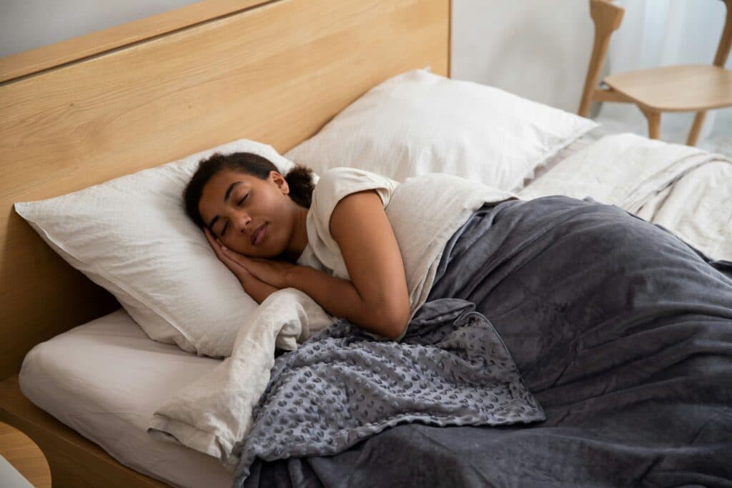 neck pain from sleeping, Image of a woman sleeping comfortably in bed, with both her hands placed under her head.