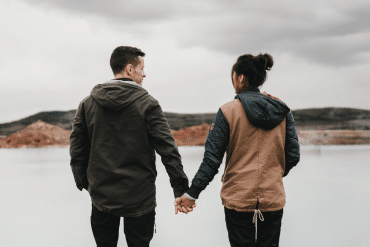 Image of a couple holding hands overlooking a lake and hills.