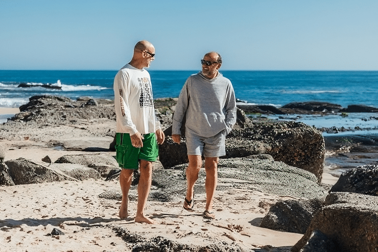 Image of two men walking side by side on a rocky beach.