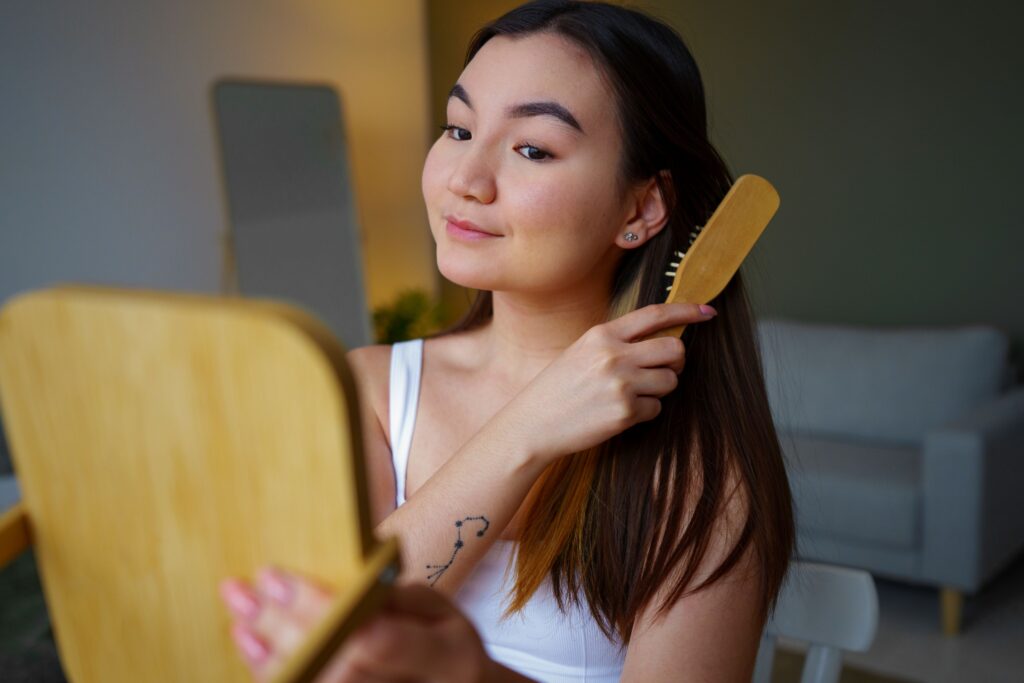 PRP hair treatment, Image of a happy woman holding up a mirror with her left hand and brushing her hair with her right hand.