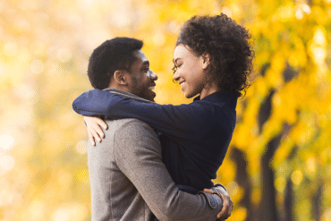 Image of a happy couple in embrace with yellow trees in the background.