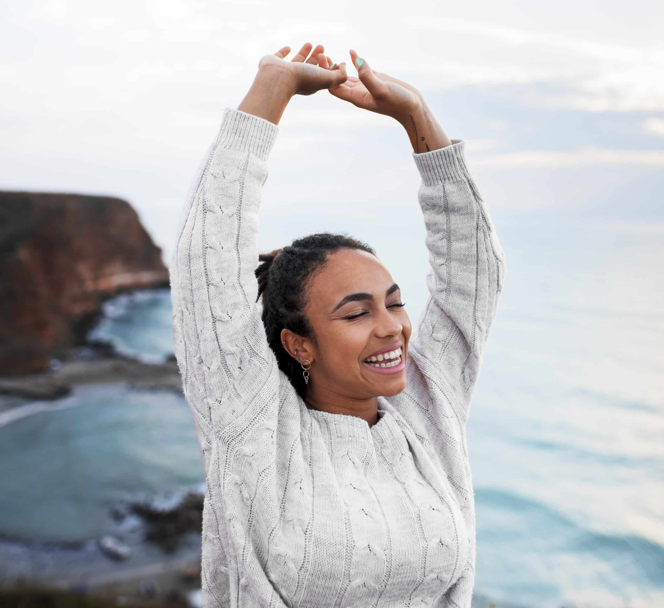 ozone therapy atlanta, Image of a happy woman stretching her arms above her head with a cliff and the ocean in the background.