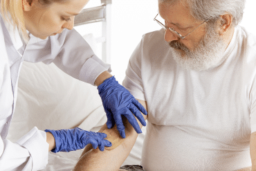 Image of a female doctor inserting an IV needle into a male patient’s right arm.