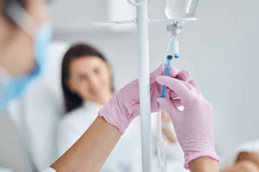 Image of a doctor adjusting an IV drip with a female patient in the background.