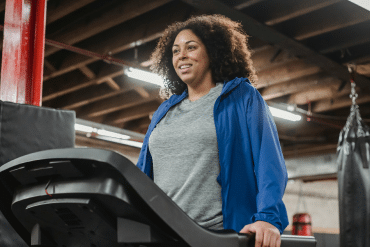 Image of a woman wearing a gray t-shirt and blue zip-up sweatshirt walking on a treadmill.