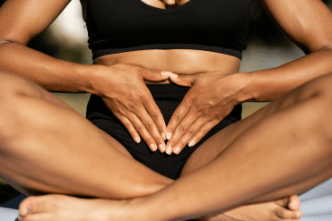 Image of a woman sitting on the ground with her legs crossed and her hands over her stomach.