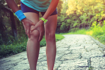 Image of a woman jogger grasping her right knee with both of her hands.