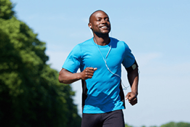 Image of a happy man running outside, wearing a blue t-shirt and ear pods.