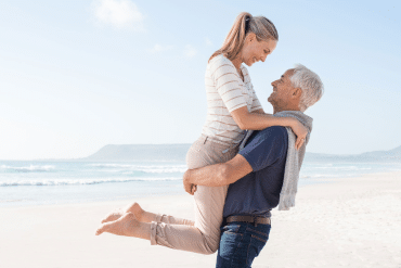 Image of a man lifting a woman while happily looking at each other on the beach.