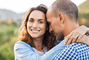 Image of a smiling woman embraces a happy man with is eyes closed.