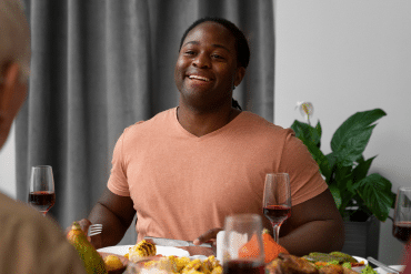 Image of a man sitting at a table with food and other people.