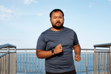 Image of a man jogging on a boardwalk next to the ocean.