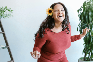 Image of a smiling woman wearing a red long sleeve dress and a sunflower in her right ear.