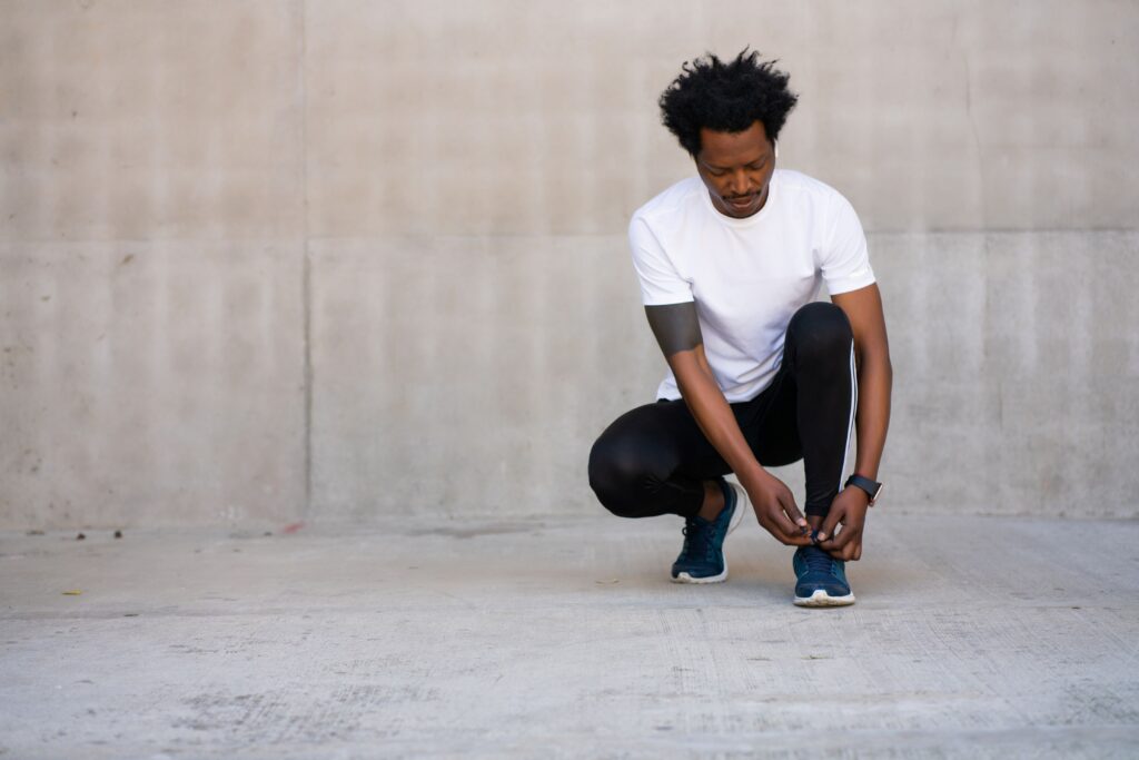 Orthopedic stem cell therapy, image of a runner squatting down to tie the sneaker on his left foot.