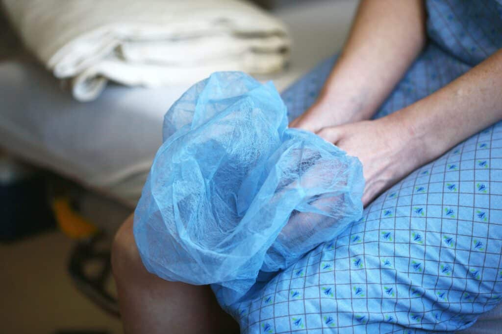 Unnecessary spine surgeries, image of a patient sitting on a hospital gurney in a hospital gown, holding a hair net in their hands.