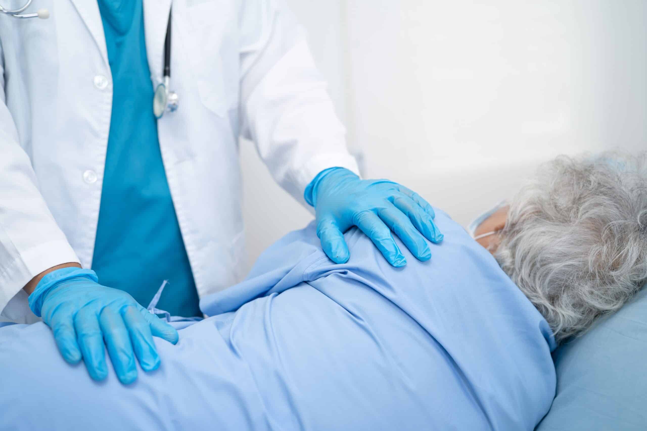 Unnecessary spine surgeries, image of an elderly patient laying on their right side on a hospital bed with a doctor standing over them and the doctor’s hands placed on the patient.