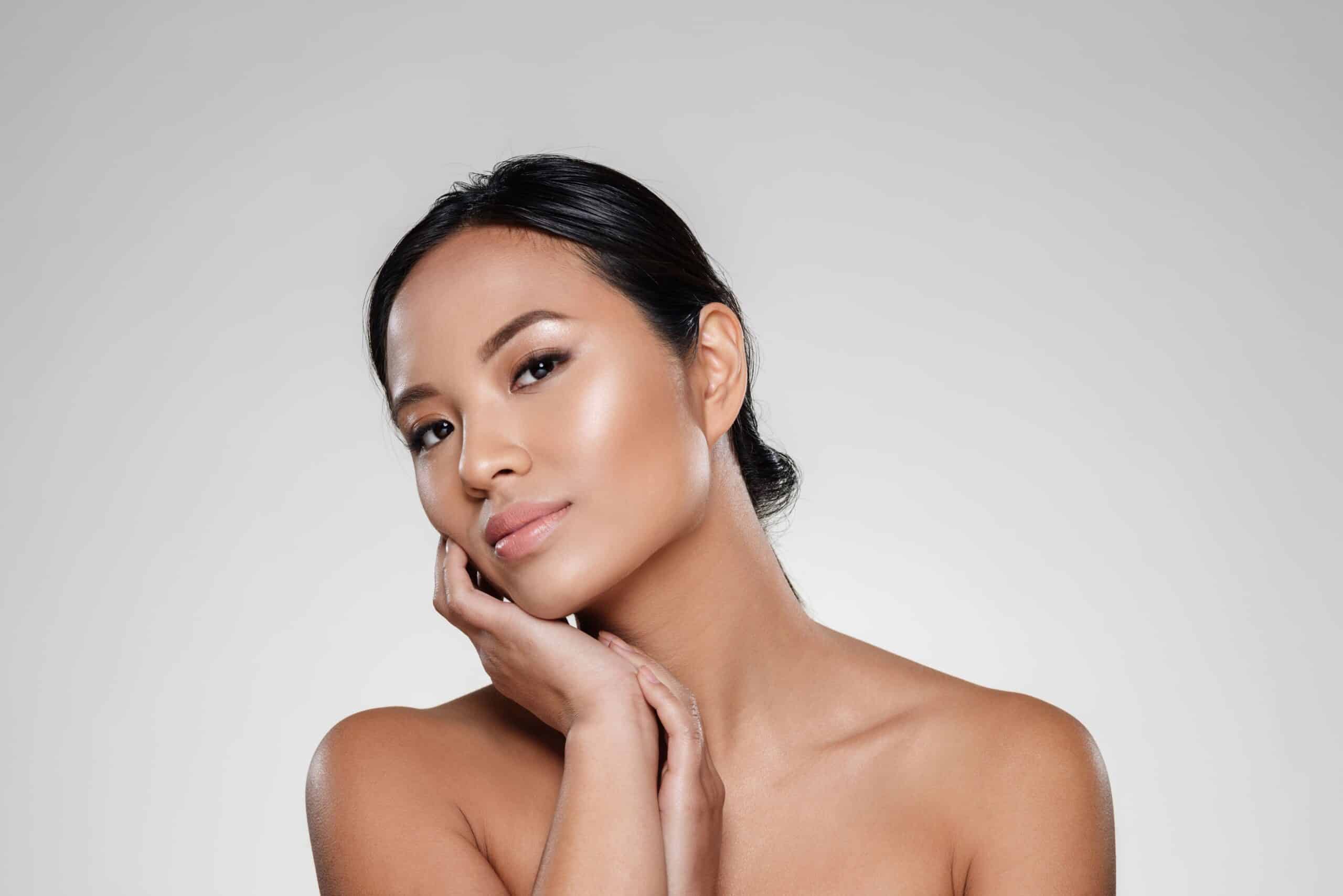 What is a Vampire Facial®, image of a young asian woman with a glowing face, holding her hands to her face.