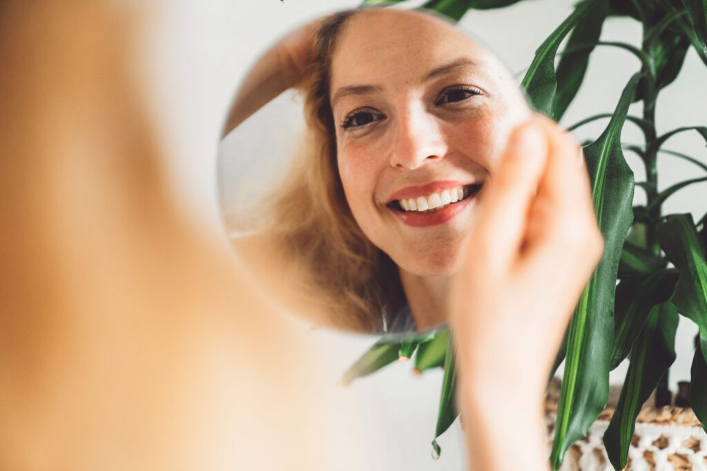 What is a Vampire Facial®, image of a happy woman holding a circular mirror and smiling into it.